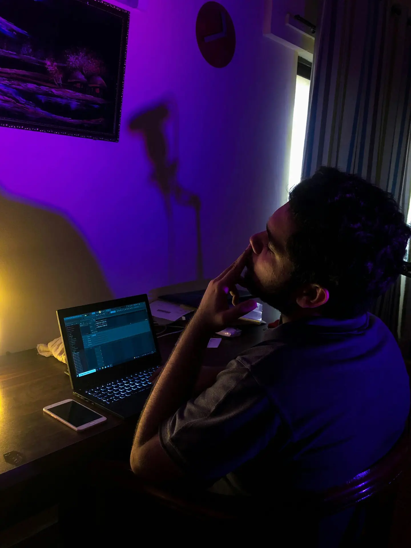 A man sitting at a desk with a laptop under moody lighting setup, evoking late-night work vibes.